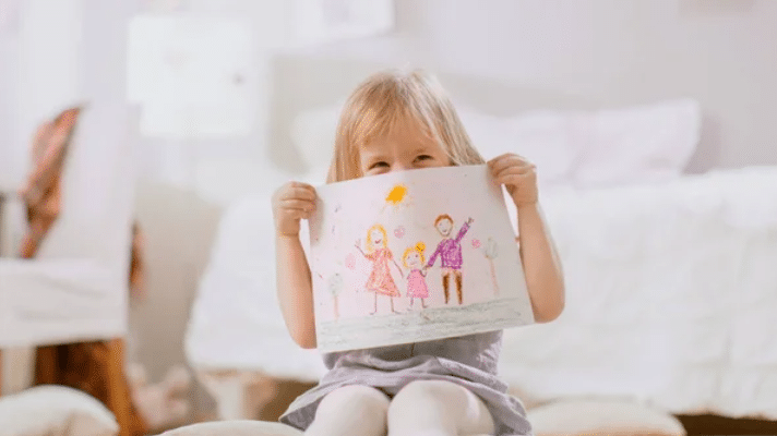 child showing her drawing while smiling