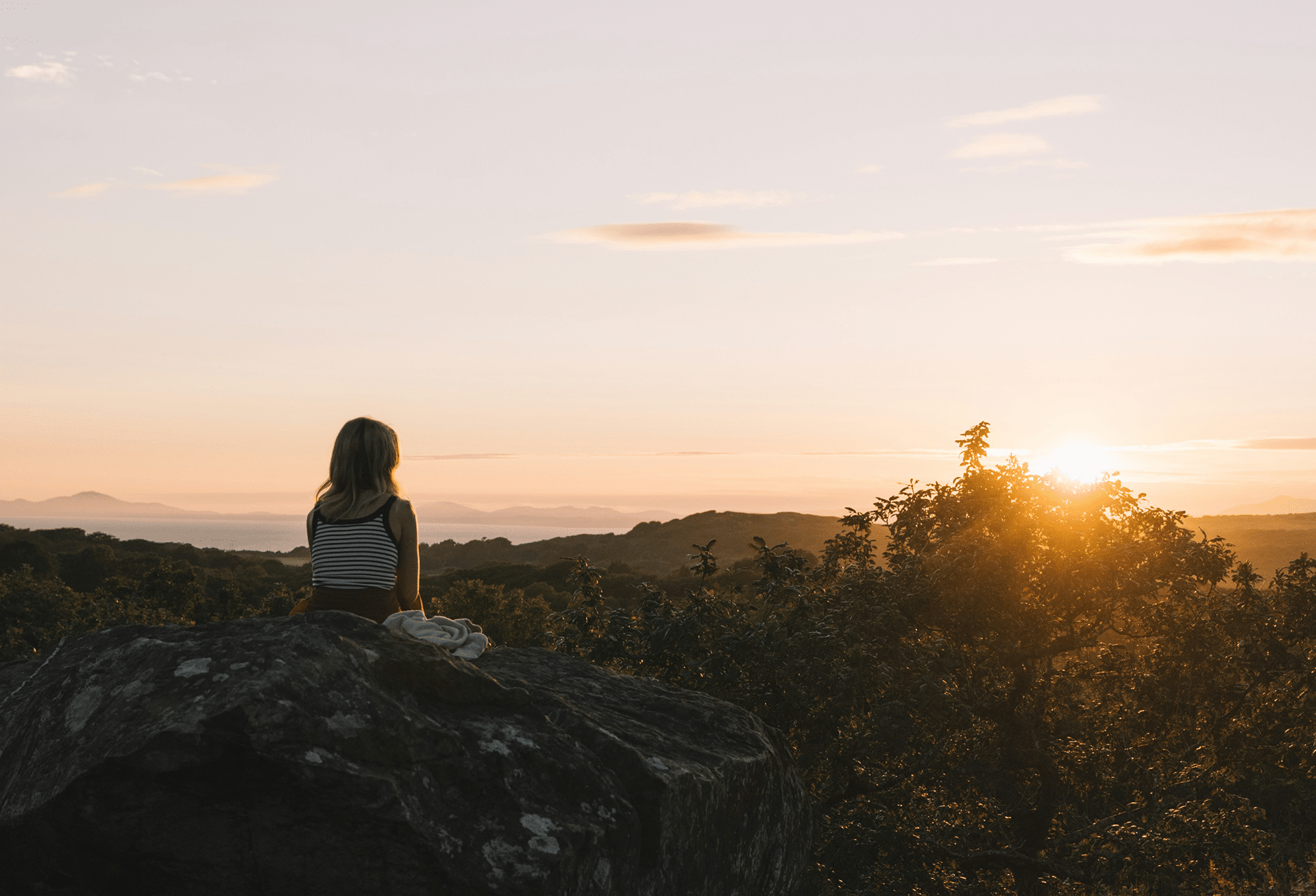 Woman sitting on a rock at sunset in quiet reflection