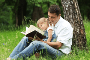 Father reading a book with his young daughter outdoors, reflecting faith-centered family learning at Coker Early Learning Center in San Antonio