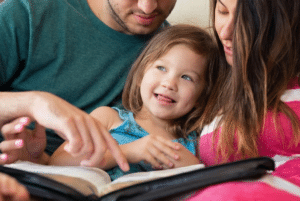 Parents reading a book with their young daughter, reflecting faith-based learning at Coker Early Learning Center Kindergarten in San Antonio